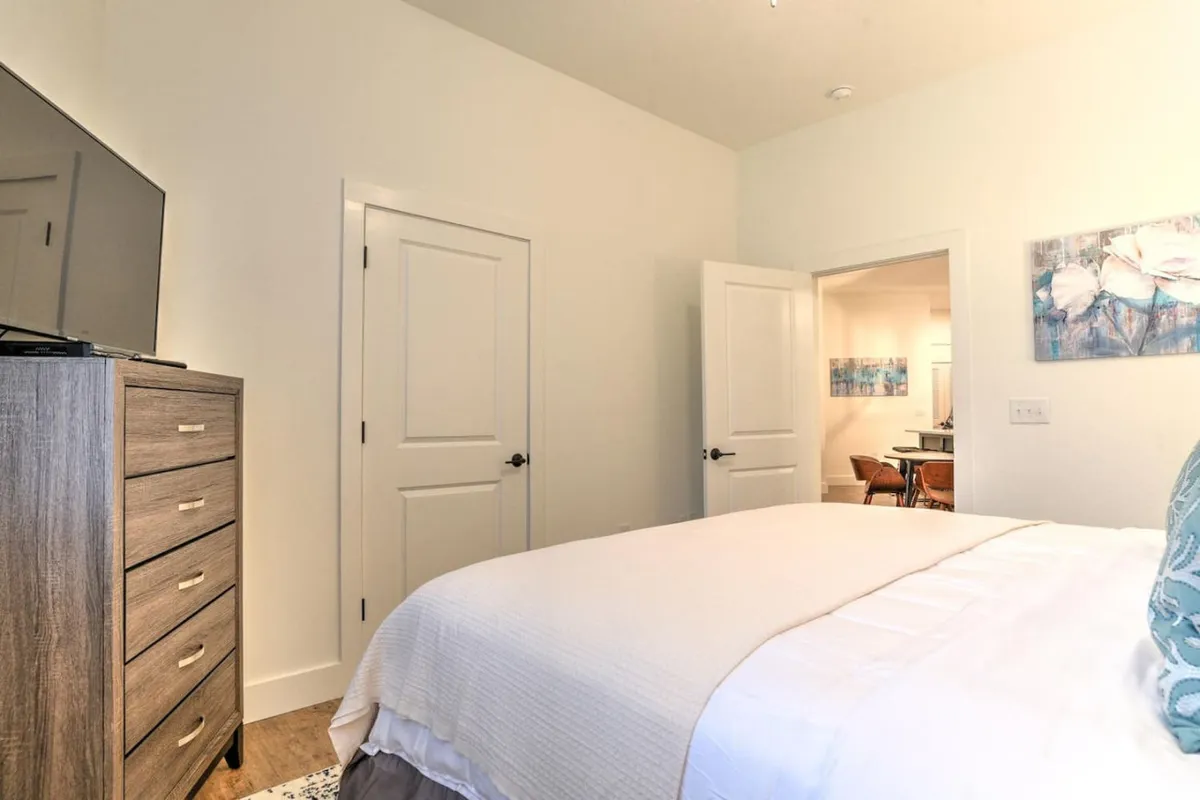 A serene bedroom featuring a plush bed, stylish dresser, TV, and local artwork. The space feels restful yet connected to the energy of the city, ideal for unwinding after experiencing Asheville’s nightlife.