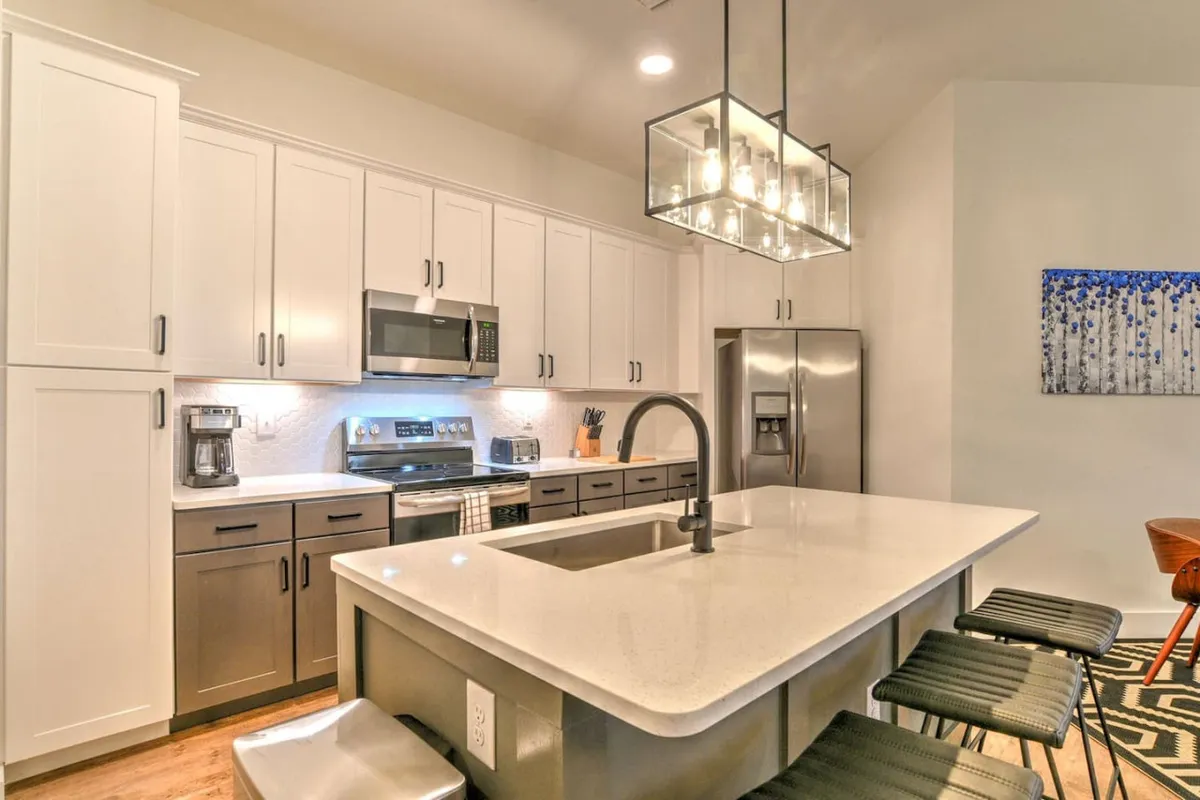 A bright, inviting kitchen with a large island, modern lighting, stainless steel appliances, and colorful artwork on the wall. The open layout suggests easy transitions from indoor living to the excitement found just outside.