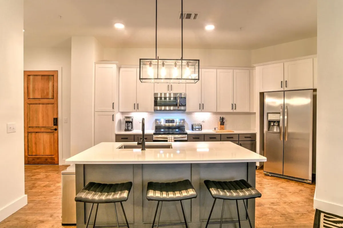 This image spotlights the kitchen’s island countertop with stools, gleaming stainless steel appliances, and stylish lighting. The layout hints at a spacious, open-concept area ideal for both cooking and casual gatherings. The inviting atmosphere is underlined by hints of culinary activity and the warm presence of family or friends.