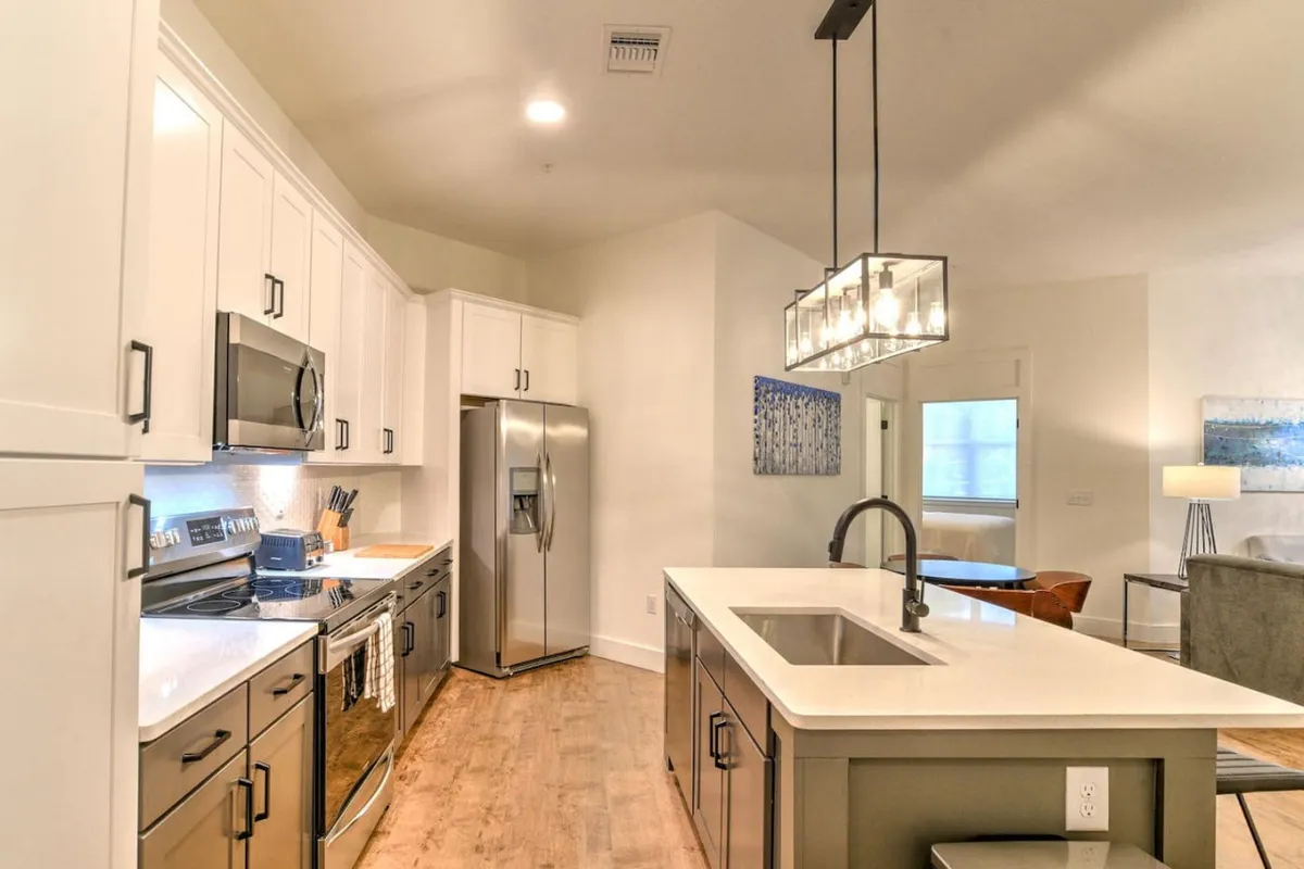 This perspective showcases a kitchen island with modern lighting and prominent stainless steel appliances, plus a glimpse of wall artwork that adds a personal touch. The area is staged for cooking and entertaining, suggesting a lively, comfortable environment for anything from quiet breakfasts to festive dinners.