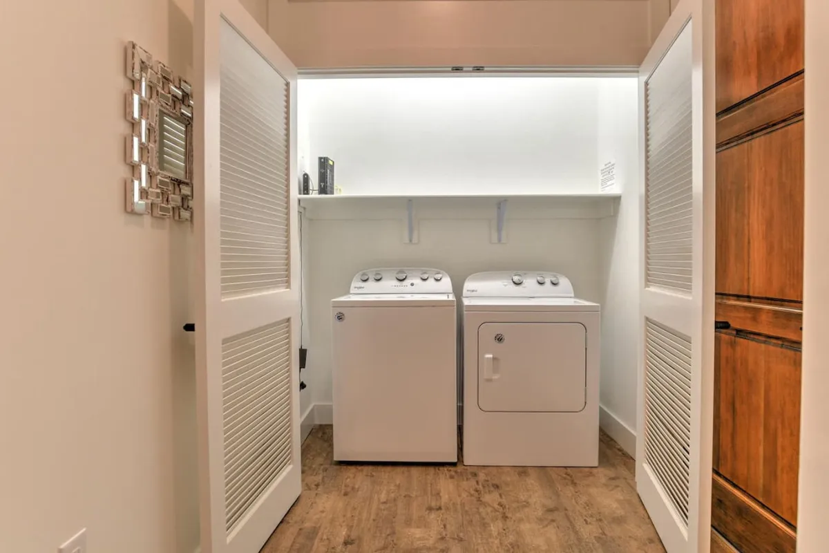 This image depicts a clean, well-organized laundry area with a washing machine, dryer, and storage shelf. The practical, tidy space conveys a sense of modern convenience and attention to functional amenities within the property.
