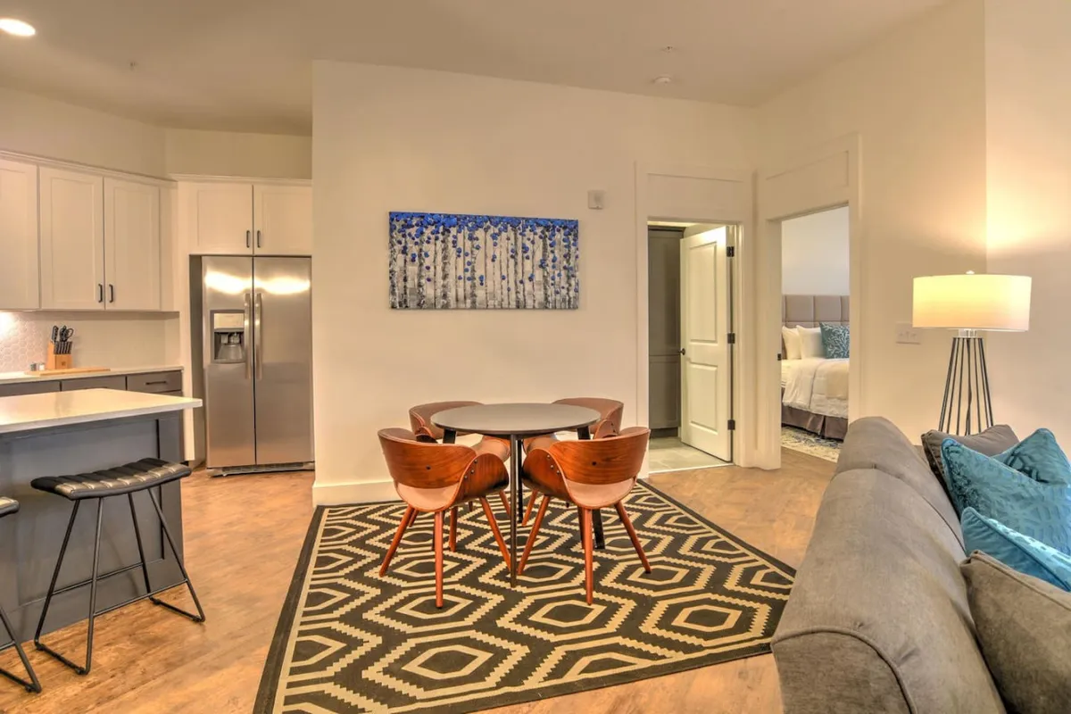 A cozy, open-plan area featuring a round dining table with stylish chairs, abstract wall art, and a sofa with inviting cushions. The layout suggests a seamless flow between spaces, ideal for both dining and relaxed gatherings.