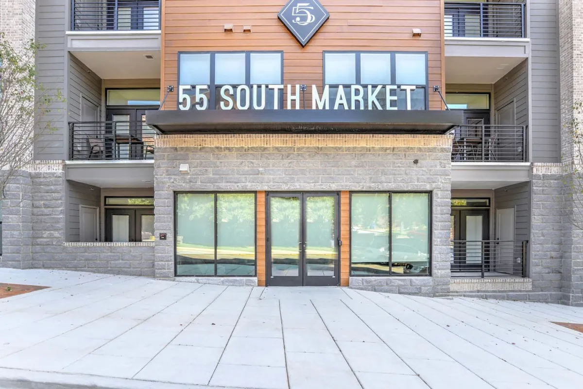 This exterior image shows the welcoming facade of the building, with a prominent entrance door and clear signage. The photo captures the modern look of the property and illustrates the direct access to the downtown environment, as well as highlighting the building’s secure and inviting entry.
